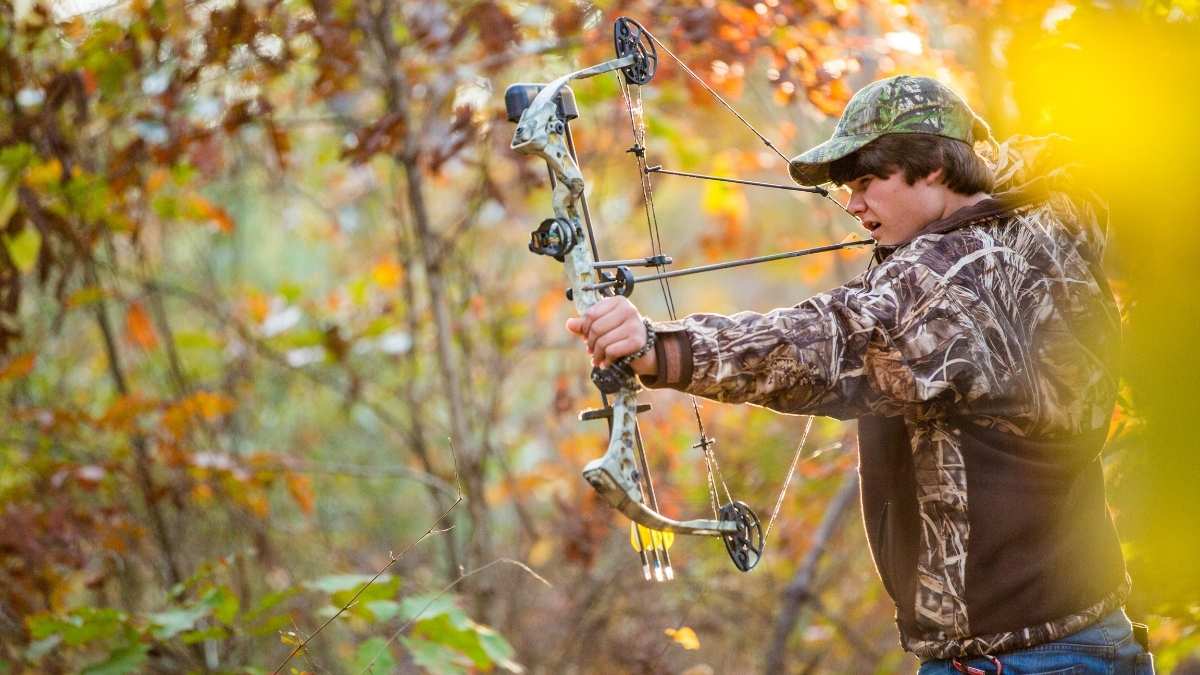 A crossbow hunter aiming in the forest -- still hunting with a bow